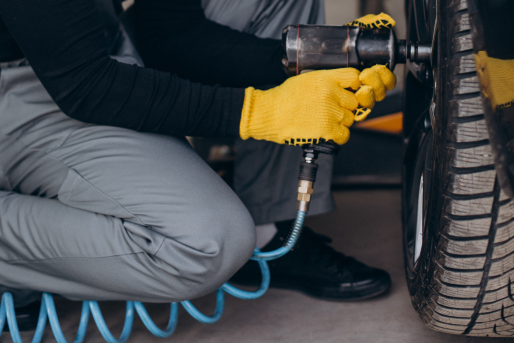 The image depicts a bustling tire shop at New Cochin Tyres in Kochi, with customers and staff engaged in various tire-related activities. A wide selection of tires is prominently displayed, showcasing the comprehensive range of tire solutions offered by the shop.